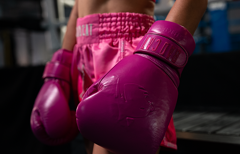 Person wearing pink boxing gloves and shorts in a blurred indoor setting