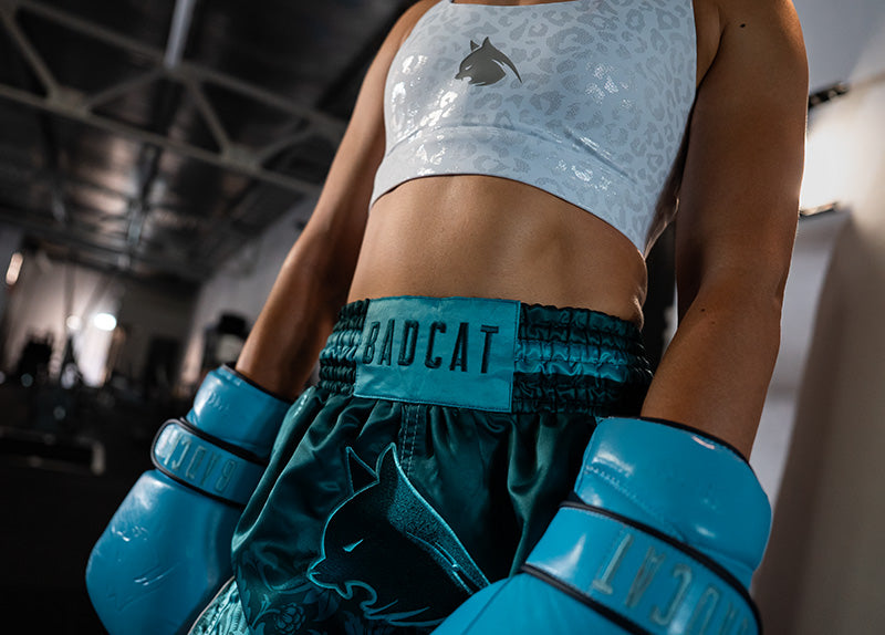 Woman wearing boxing gloves and shorts with a sports bra in a gym setting