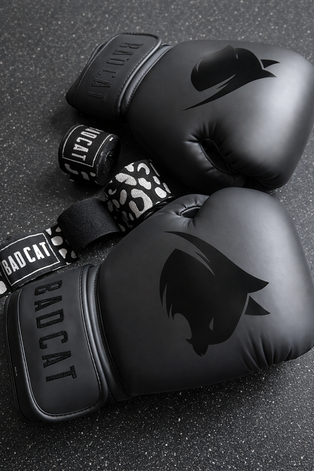 Black boxing gloves with 'BAD CAT' branding on a dark textured surface