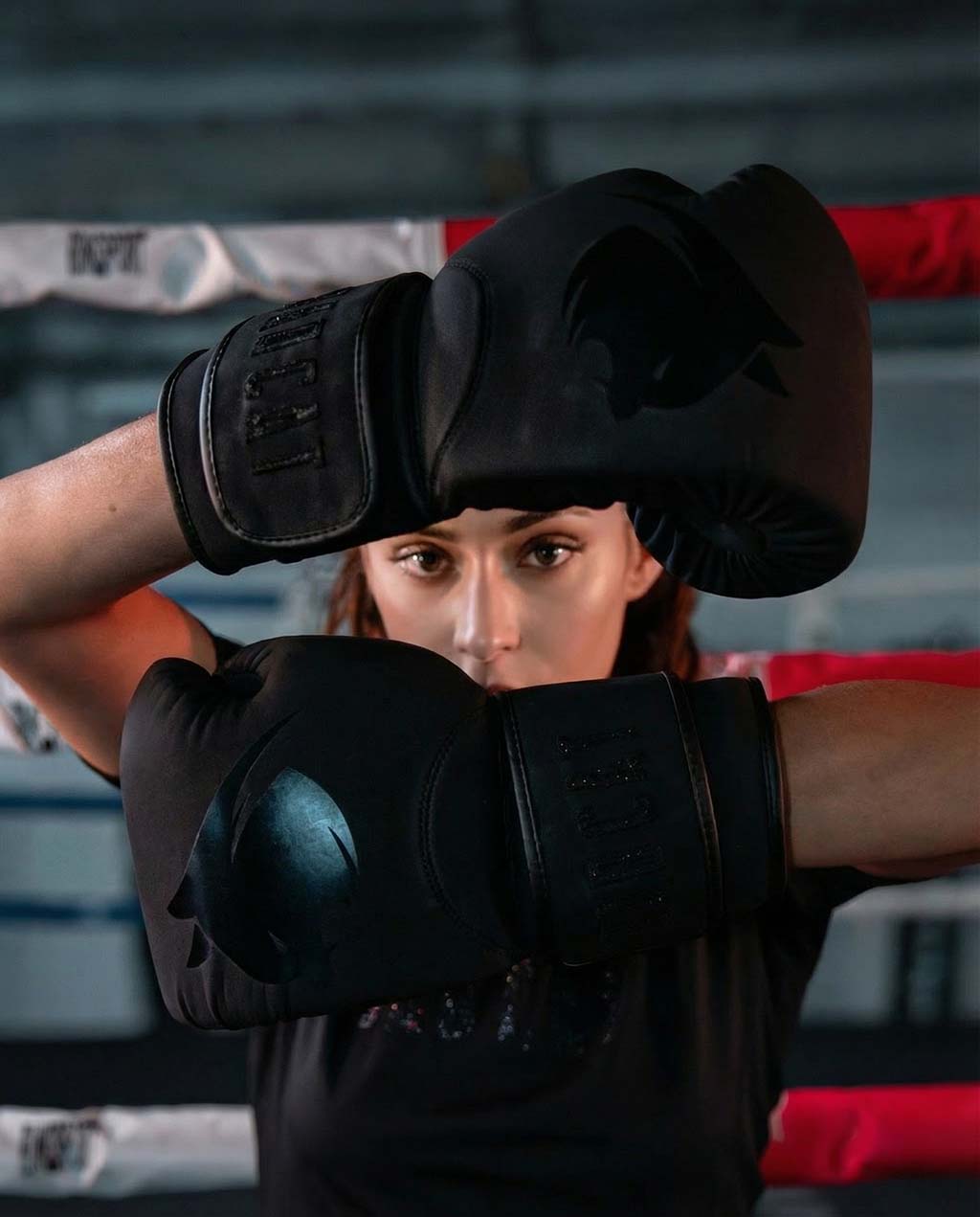 Woman wearing black boxing gloves in a boxing ring.