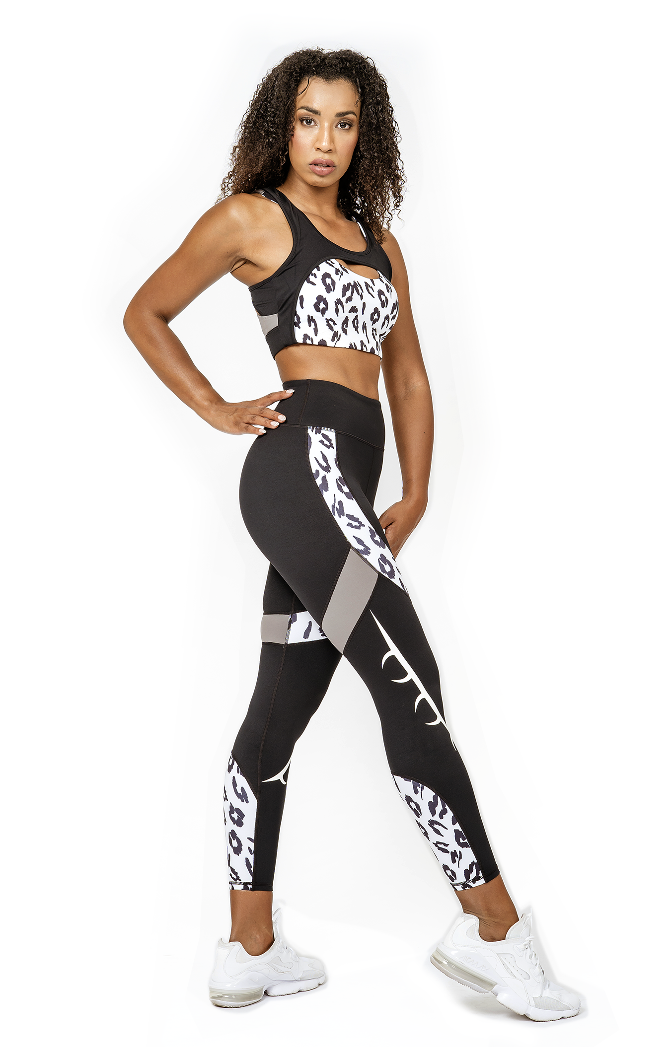 A model wearing a matching set of BAD CAT branded black and white leopard print sports bra and leggings, designed for fitness activities.