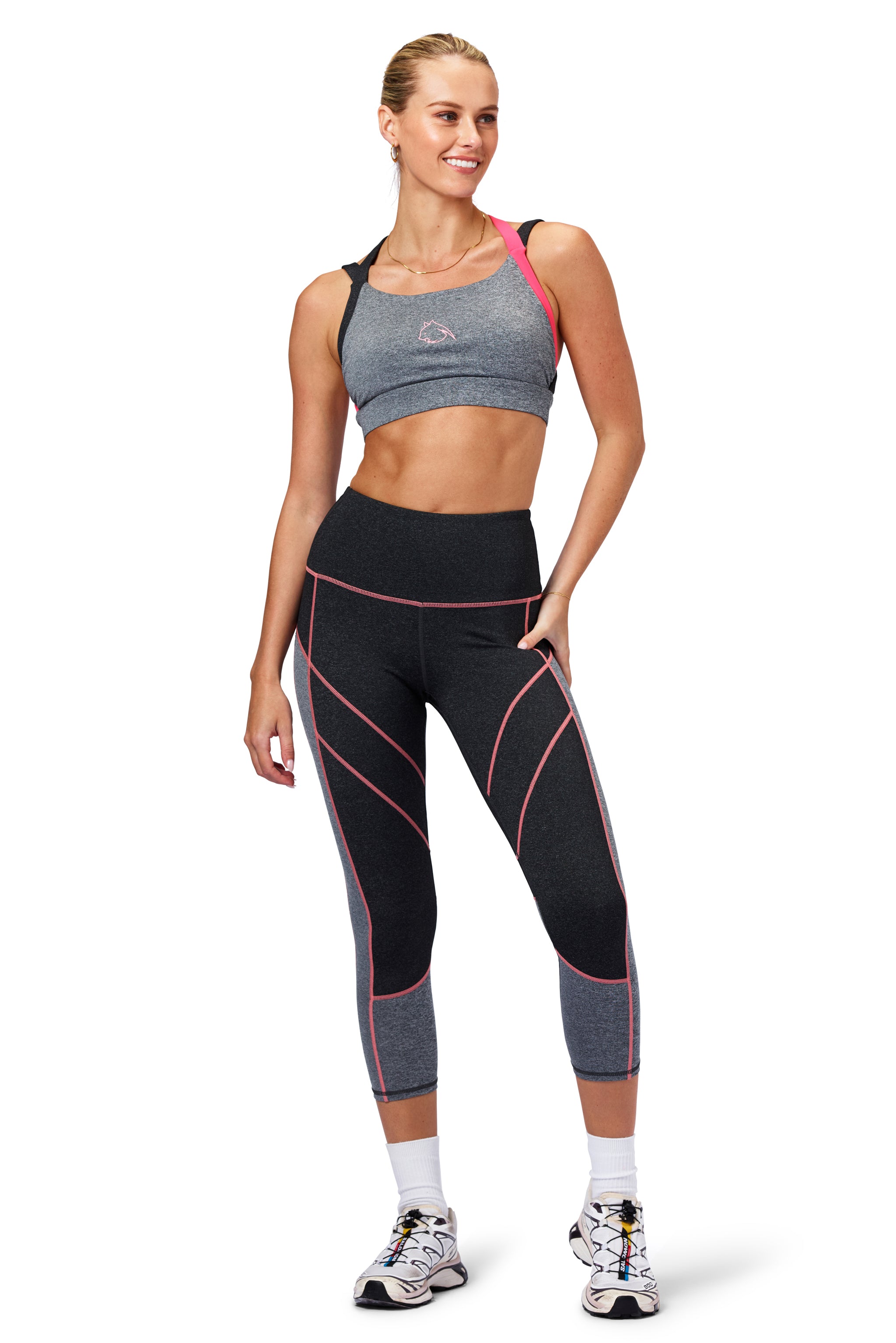 Woman wearing a gray sports bra and matching leggings with pink accents on a white background