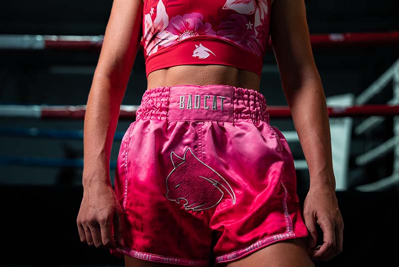 Person wearing pink athletic shorts with a logo and red top in a boxing ring.