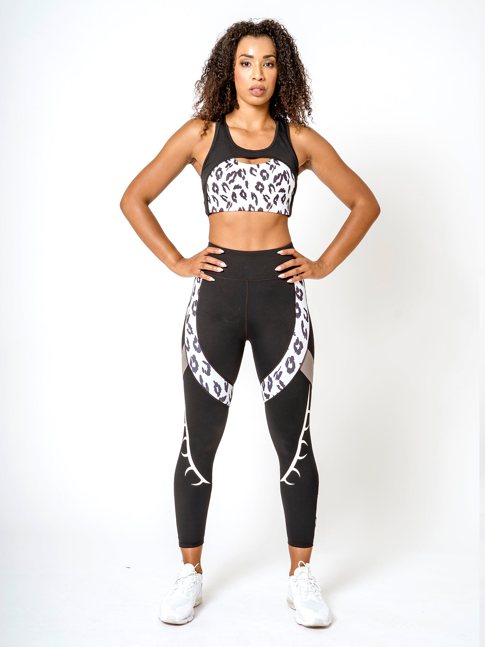 A model wearing a matching set of BAD CAT branded black and white leopard print sports bra and leggings, designed for fitness activities.