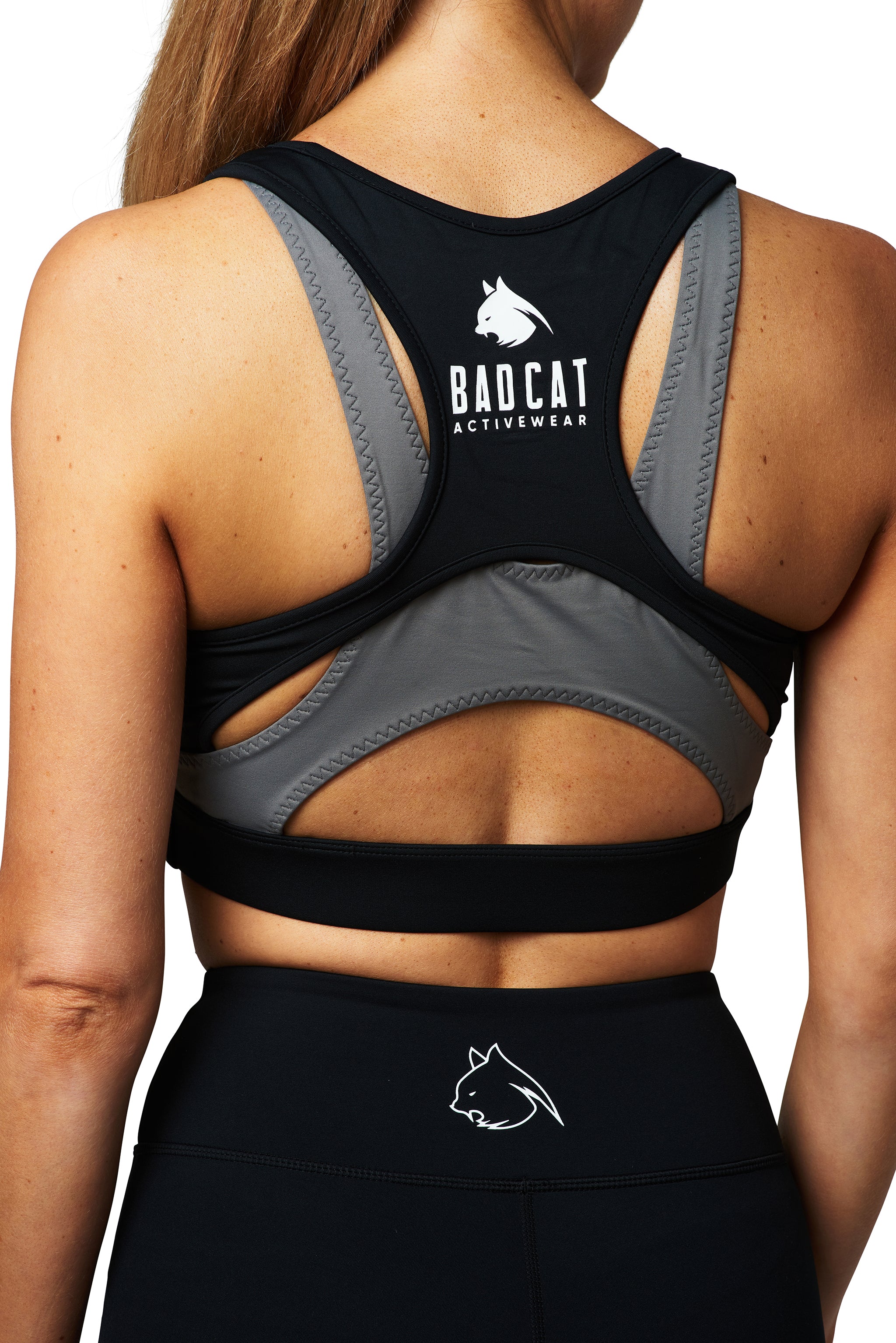 A woman wearing a BAD CAT branded black and white leopard print sports bra, paired with black activewear leggings, pictured from behind.