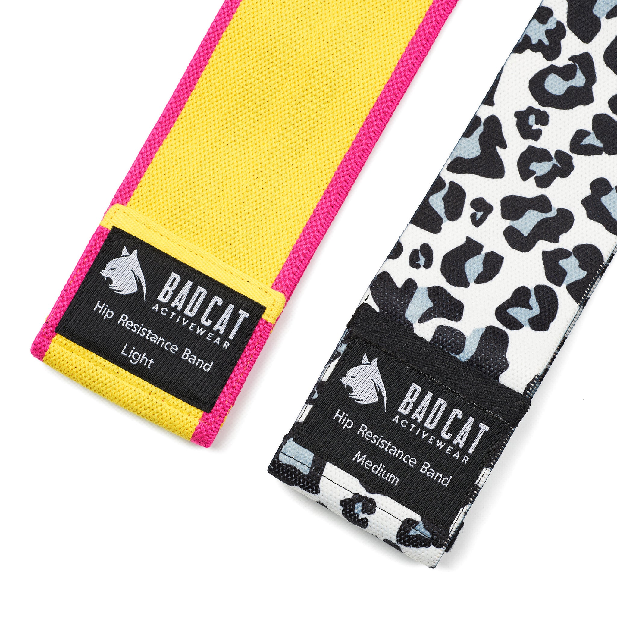 Two resistance bands with 'BAD CAT' branding, one yellow and one with a black and white animal print. The yellow band is labeled 'Hip Resistance Band Light' and the animal print band is labeled 'Hip Resistance Band Medium'.