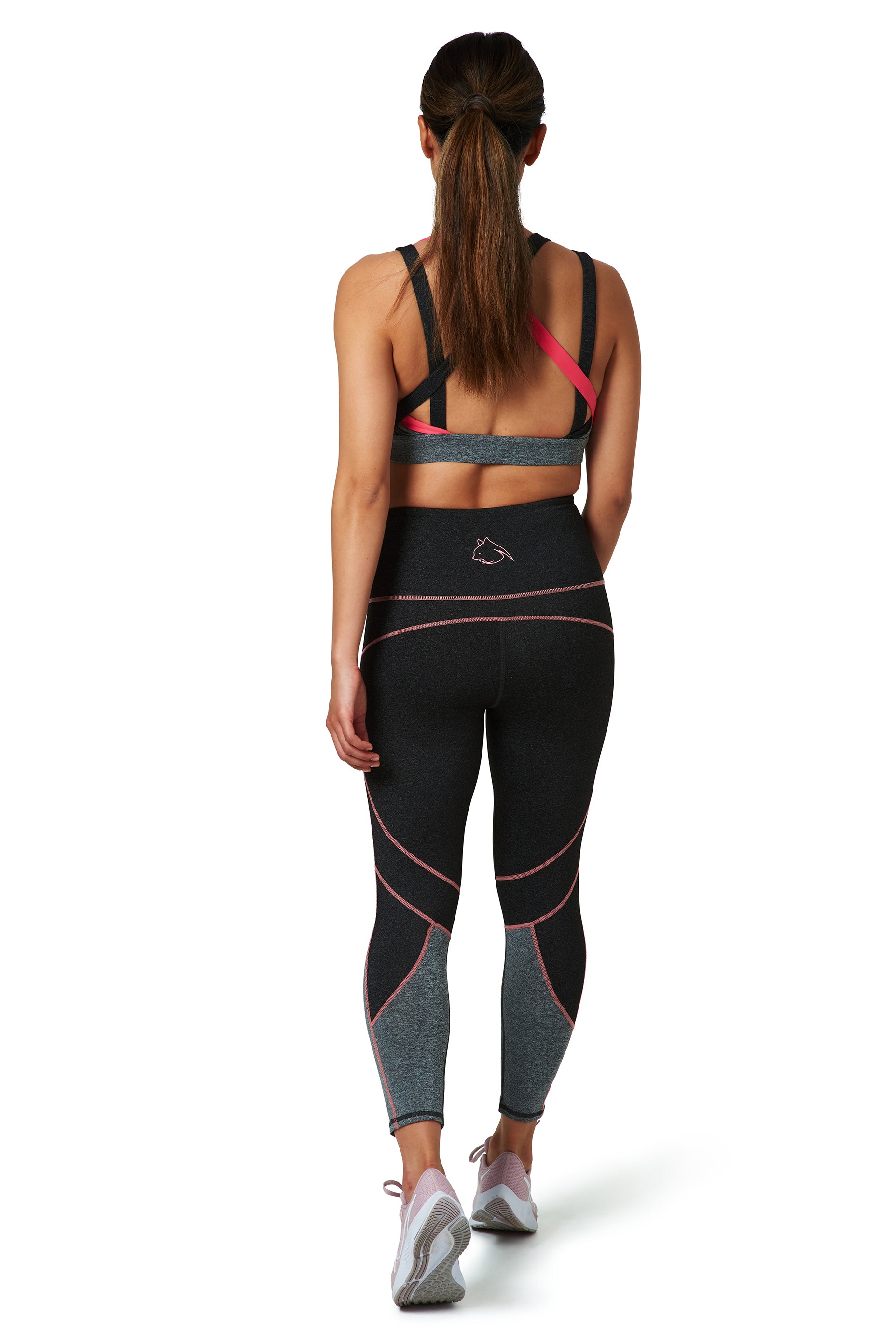 A woman is standing, wearing grey and pink BAD CAT activewear leggings with a wide waistband and a matching sports bra, pictured from behind.